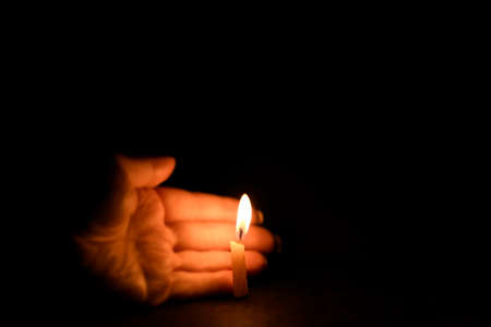 A candle burns in the dark. The light from the candle illuminates the palm. A woman's hand supports...