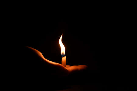 Candle in hand. Small candle with a curved flame. Complete darkness. The candle is in the palm of your hand.の写真素材
