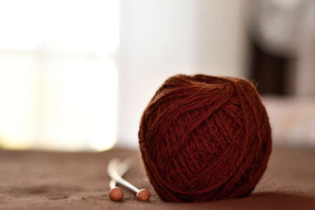 A ball of brown woolen threads and two wooden knitting needles close-up. Preparation for knitting.