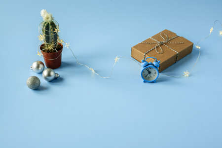 Cactus decorated with Christmas lights gift box and alarm clock on blue background