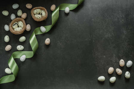 Colourful Easter eggs with birds nest and green satin ribbon on dark bakcground