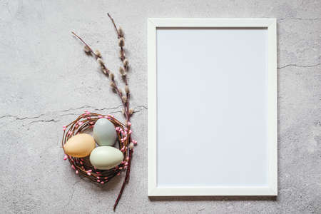 Easter minimal background with white picture frame, Easter eggs in birds nest and pussy willow catkin branches. Happy Easter greeting card with copy spaceの写真素材