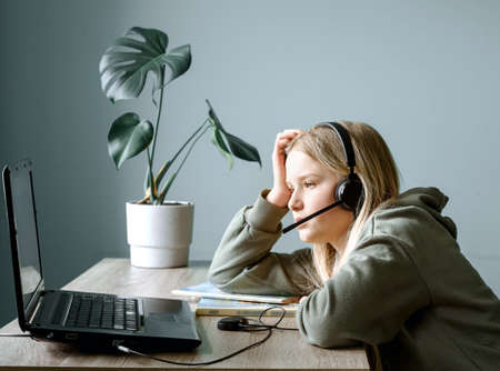 Teenage girl in headphones with microphone studying online at home, remote learning and home...