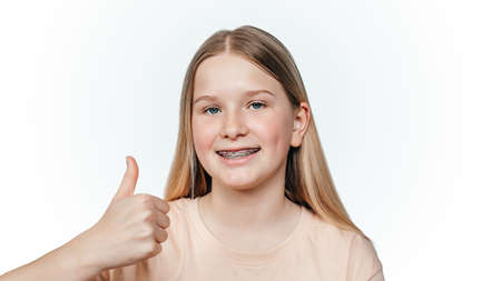 Smiling blonde girl with orthodontic braces holding her thumb up, orthodontic treatment of...
