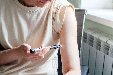 Diabetes woman injects insulin in her arm with insulin pen needle, diabetes patient makes an arm subcutaneous insulin pen injection at home, diabetes world day.の写真素材