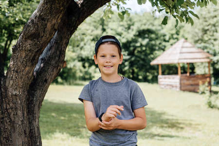 A happy young boy wearing his hat backwords under a tree in the countryside, summer rural backgroundの写真素材