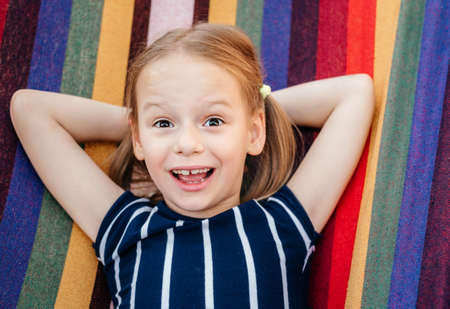 Happy little girl with crooked baby teeth in the colorful hammock summer background, summer holiday outdor activitiesの写真素材