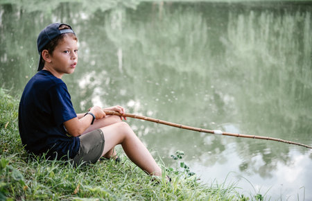 A boy holding a fishing rod and fishing in the lake, summer activities and hobbies for childrenの写真素材