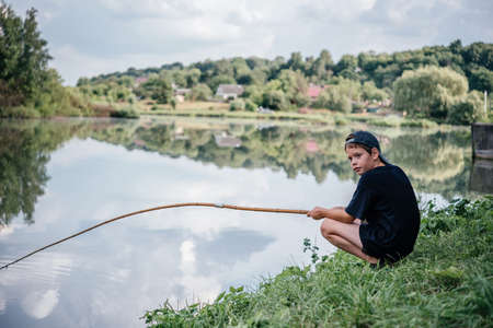 A boy holding a fishing rod and fishing in the lake, summer activities and hobbies for childrenの写真素材