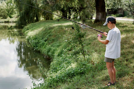 A boy holding a fishing rod and fishing in the lake, summer activities and hobbies for childrenの写真素材