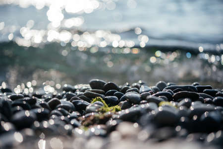 Beach pebbles with sparking sun bokeh and foamy sea wavesの写真素材