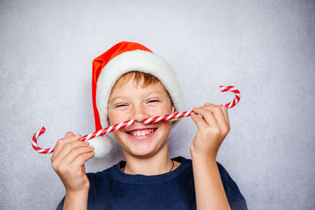 Playful boy in Santa hat making moustache with candy canes during Christmas and New Year holidaysの写真素材