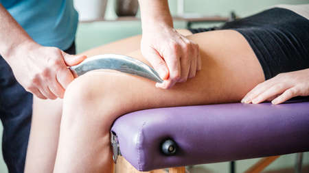Therapist using IASTM instrument for soft tissue treatment on the leg of a female patientの写真素材