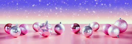 Pink and purple Christmas tree bulbs on purple background with falling snow, banner sizeの写真素材