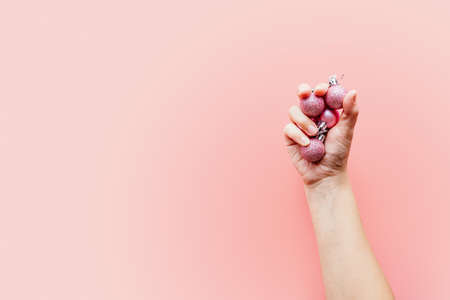 A hand holding pink glitter Christmas balls on pink backgroundの写真素材