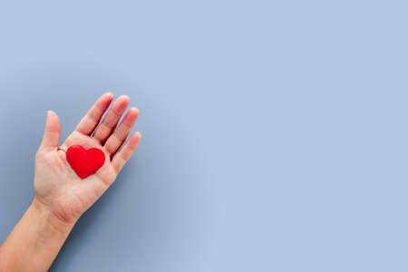 A hand holding a red fabric heart on blue background, Valentines day backgroundの写真素材
