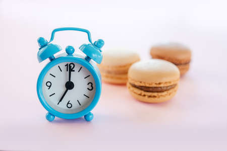 Blue alarm clock and vanilla, mocha and chocolate macarons on pink background
