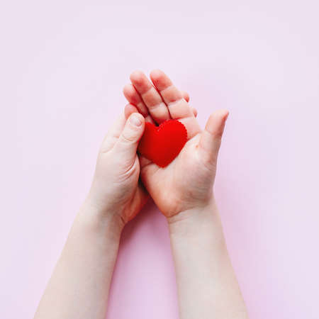 Childs hand holding a red fabric heart on pink background with copy space, Valentines day backgroundの写真素材
