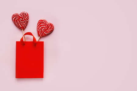 Red shopping bag with two heart shaped lollipops on pink Valentines day backgroundの写真素材