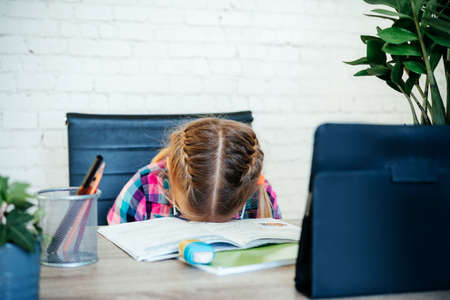 Tired child put her head on the table while having online lesson, distance learning for childrenの写真素材
