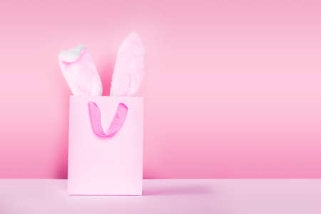 Easter shopping composition with bunny ears out of shopping bag on pink backgroundの写真素材