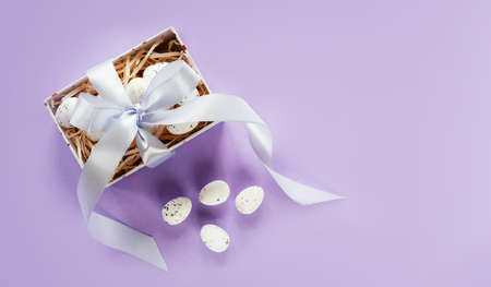 Easter creative layout with Easter eggs in a gift box with lavender blush ribbons on pale purple...