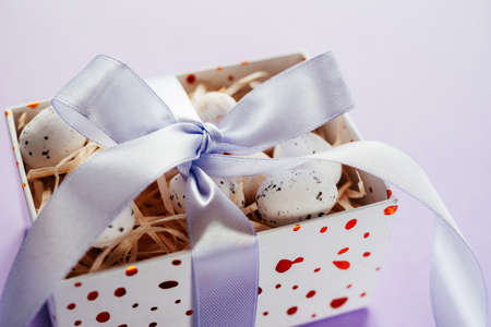 Easter creative layout with Easter eggs in a gift box with lavender blush ribbons on pale purple backgroundの写真素材