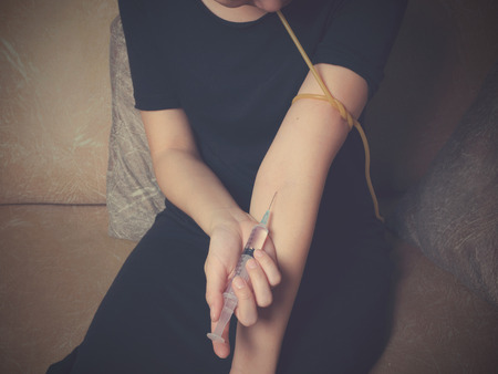 Female using syringe, female drug addict sitting in the background with vintage toneの写真素材