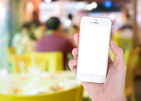 Woman hand showing smart phone with isolated screens display on blur of restaurant backgroundの写真素材