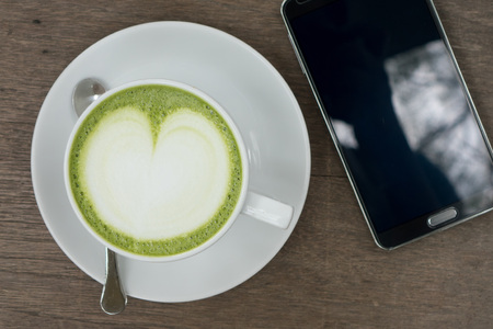 Green tea latte on wood background with the blank screen smartphone