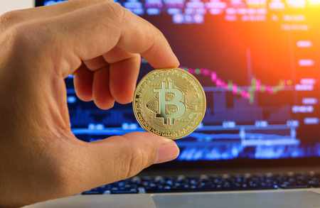 Hand holding golden Bitcoin on chart backgroundの写真素材