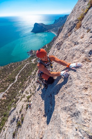 The climber climbs the rock with sea on background.の写真素材