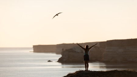 Girl on cliff above the sea at sunset.の写真素材