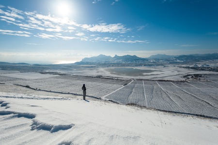 Girl on the snowy slope with mountains and the sea on background.