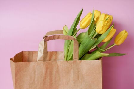Yellow tulips bouquet in brown paper bag on rose color backgroundの写真素材