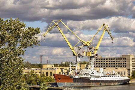 Big ship with rusty sides moored at the pier. Large port cranes form the letter W against a blue sky...