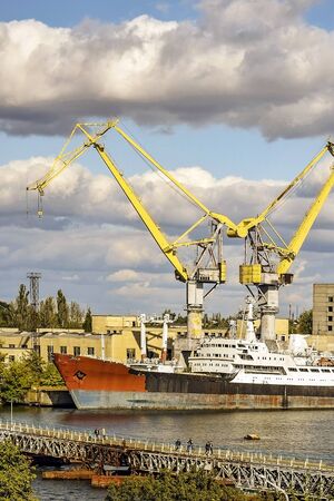 Big ship with rusty sides moored at the pier. Large port cranes form the letter W against a blue sky with heavy dark clouds. Selective focus. Copy space.の写真素材