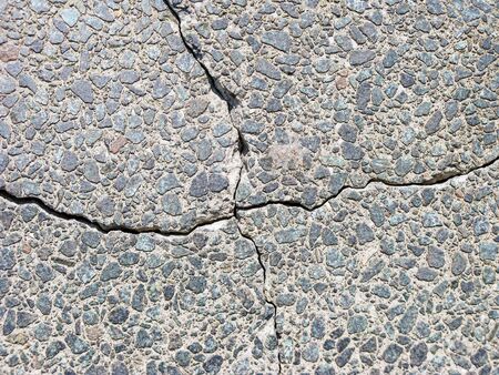 Deep crack in the form of a cross on a road surface with granite stones. A square divided into four...