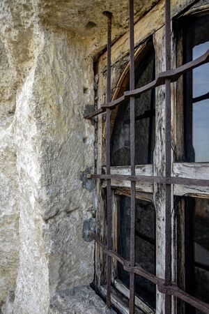 Wooden window of an ancient rock monastery. Protected by forged metal bars. Rusty iron. Close-up. Selective focus.の写真素材