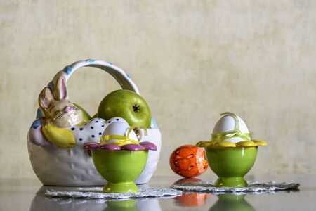 Easter setting: basket with Easter bunny, white eggs tied with ribbons of green and yellow, ceramic...