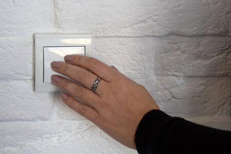 Female hand pushes button of white Switch on brick wall. Close-up. Selective focus. Copy space.