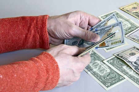Caucasian man's hands counting dollar banknotes on gray surface. Male holding money currency of United States on gray background. Close-up. Selective focus.の写真素材