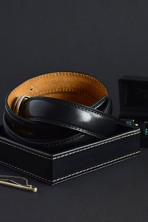 Twisted men's leather belt in black in a box on dark background, elegant accessories, close-up....