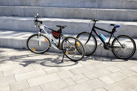 Two bicycles are parked on large concrete steps. Shadows from bicycles fall on paving slabs. Without people. Close-up. Selective focus. Copy space. の写真素材