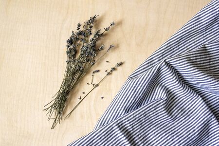 Bouquet dry lavender and linen cloth with gray stripes lie on light wooden surface. Top view, flat...