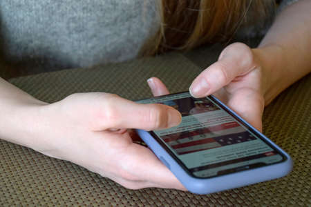 Smartphone in hands of young girl. She browses news on mobile phone screen. Mobile communications,...