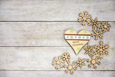Christmas toys (heart with inscription "Merry Christmas" and wooden snowflakes) on old wooden background. Winter concept, new year decorations. Flat lay, top view, copy space. Selective focus.の写真素材