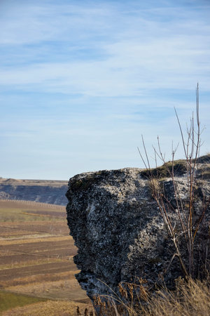 Protruding part of rock against cloudy sky and agricultural fields. Peaceful autumn rural landscape. Copy space. Selective focus. Vertical photo.の写真素材
