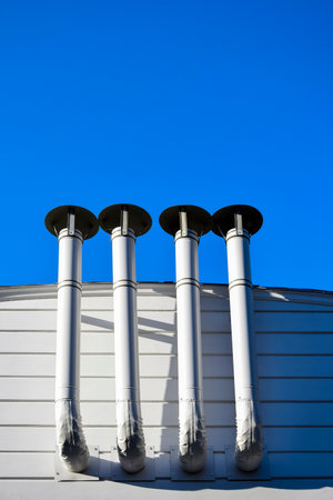 Ventilation pipes against blue sky. Building ventilation system. Fastening ventilation pipes to wall. Bottom view. Close-up. Selective focus. Copy space.の写真素材