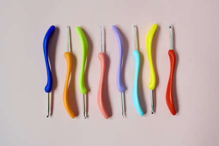 Colorful crochet hooks of different sizes on pink background. Close-up. Top view. Selective focus.